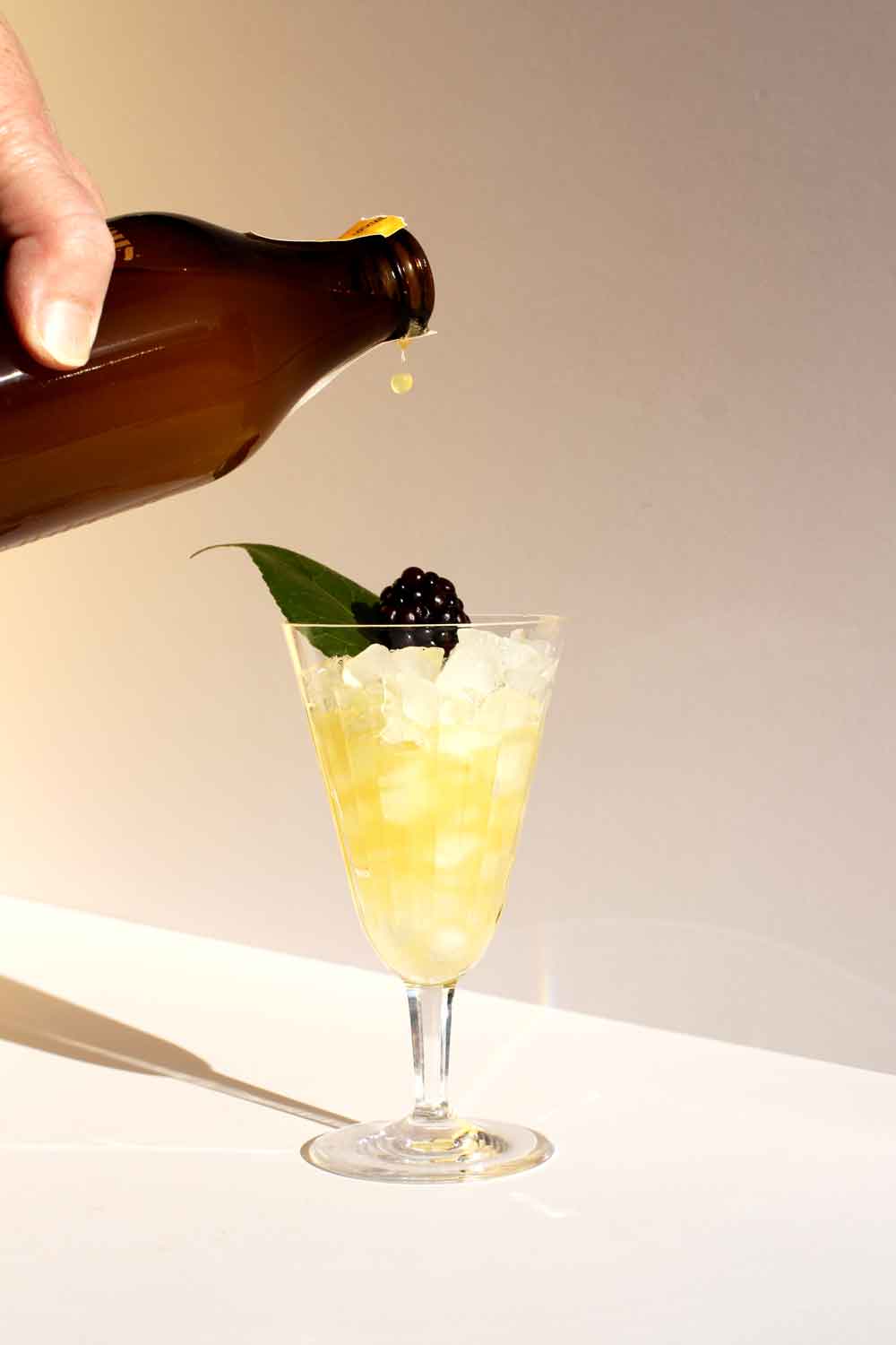 a hand pouring a bottle of Curious Elixirs into a glass