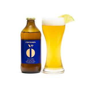 A bottle of Curious Zero Lions Mane Lager next to a filled beer glass with a lemon slice on the rim, indicating the product is a nonalcoholic craft brew.