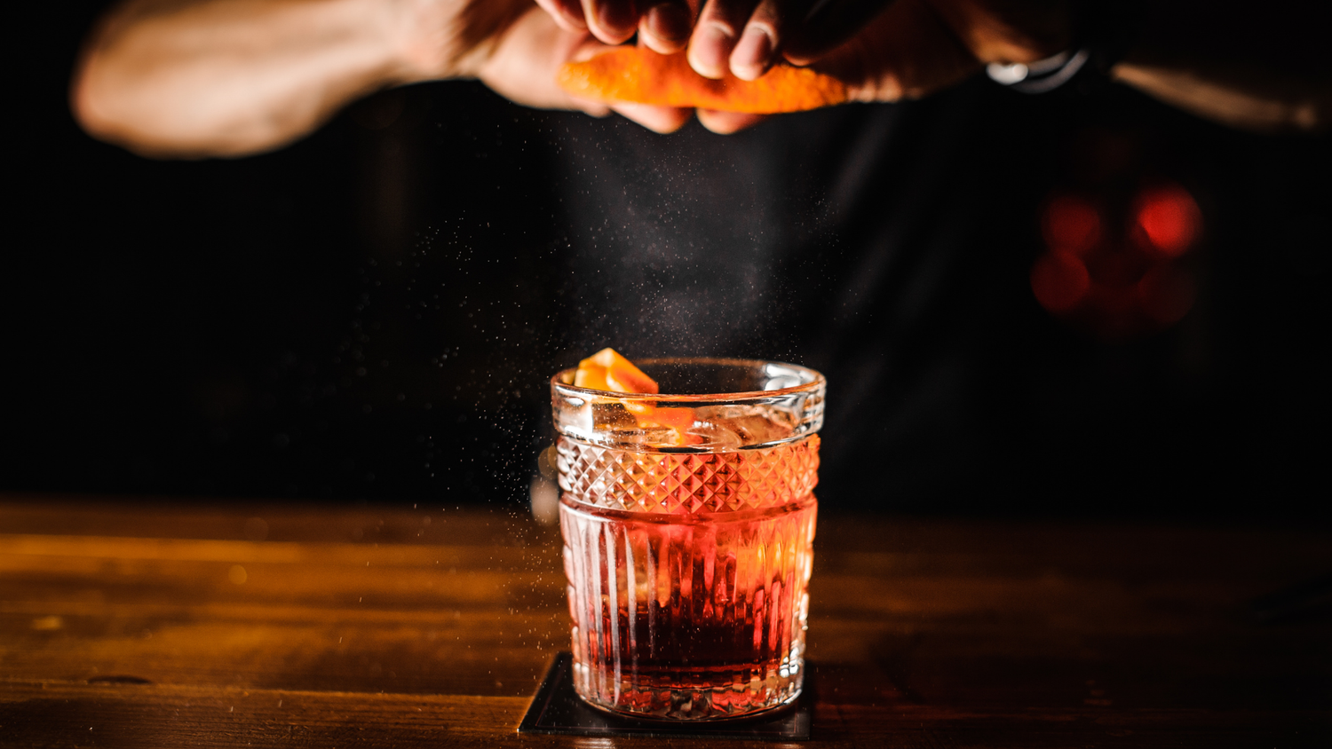 Bartender finishing a craft cocktail with a citrus peel garnish.