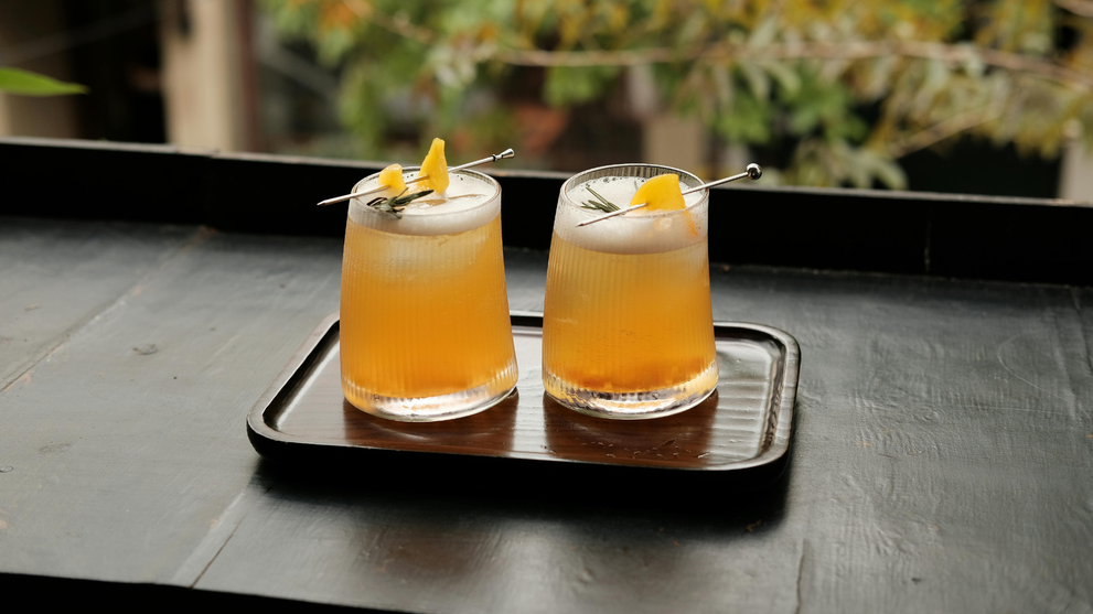 Two carefully garnished craft cocktails on a wooden tray