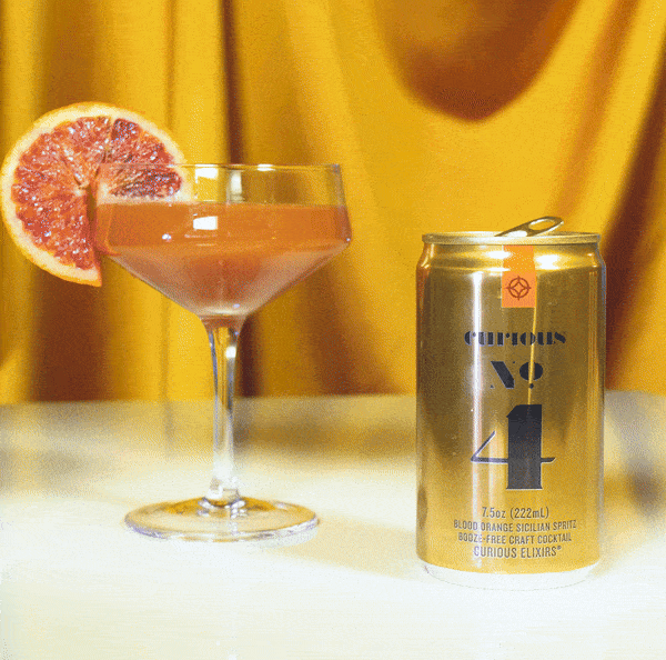 A hand with stylish nails picks up a coupe filled with Curious No. 4, leaving behind the can.