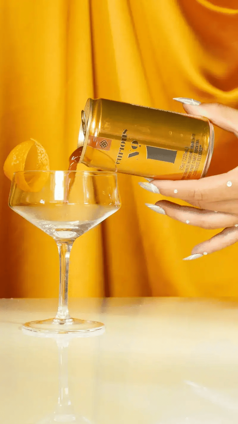 A hand with stylish nails pours a can of Curious No. 1 into a coupe.